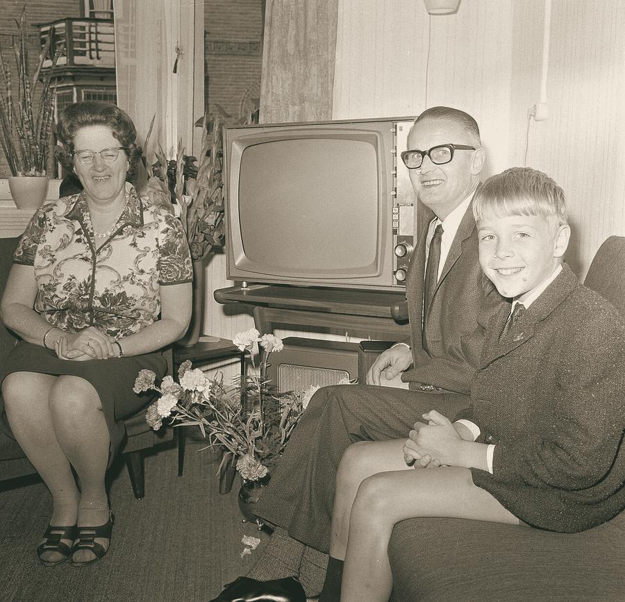 A smiling couple and their son sit beside their new television set at home.